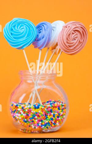 Colorful and sweet meringue lollipops on a bright orange background Stock Photo