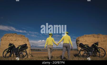 The man and woman travel on mixed terrain cycle bike touring with bikepacking. The two people journey with bicycle bags. Sport sportswear in green bla Stock Photo
