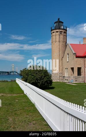 View of the Mackinaw City lighthouse with a white fence leading towards the bridge Stock Photo
