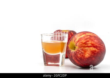 Small Shot Glass of organic Apple Cider Vinegar with the mother, two red apples is aside of the glass, image on white background. Stock Photo