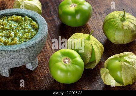Tomatillos, green tomatoes, with salsa verde, green sauce, in a molcajete, traditional Mexican mortar, on a dark rustic wooden background Stock Photo