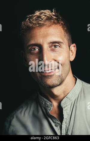 Smiling mature man portrait in studio with black background. Blond hair wearing green shirt. Stock Photo