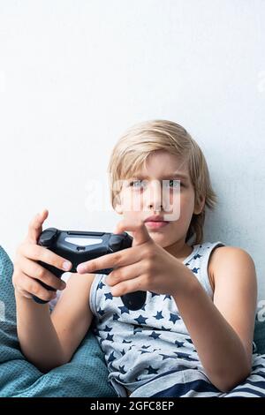 Boy holding joystick gaming controller in hands, playing video game at home. Stock Photo