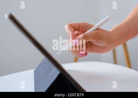 Close up woman sketching or drawing on the tablet by using a stylus pen in the white comfortable living room. Web designer or freelancer concept Stock Photo
