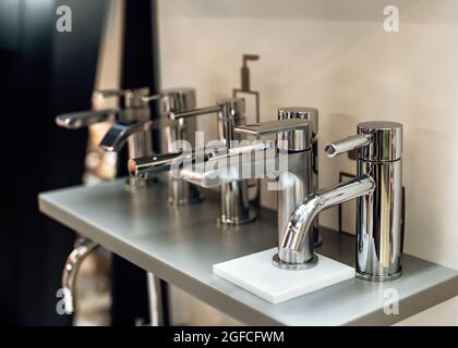 Group of modern stylish water taps for bathroom in showroom. Rows of new faucets in plumbing shop, closeup. Selective focus. Stock Photo