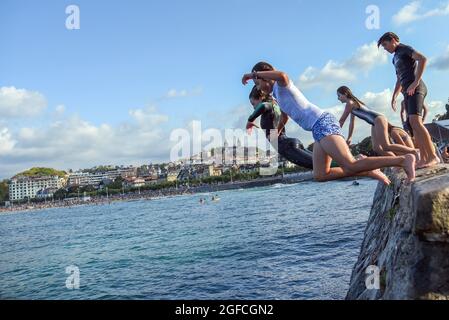 San Sebastian, Spain. 25th Aug, 2021. Young people dive into the seawater performing acrobatic jumps at La Concha Beach in San Sebastian.Young people enjoy this summer jumping into the water from the wall at the end of the promenade of Playa de la Concha de San Sebastian next to Monte Igueldo with spectacular jumps and without the danger that the stone cliffs offer for this type of jumps. Credit: SOPA Images Limited/Alamy Live News Stock Photo