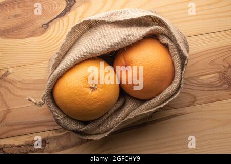 Two Juicy organic grapefruit in a jute bag, close-up, on a wooden table, top view. Stock Photo
