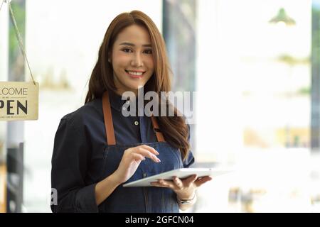 Beautiful barista image, female barista using portable tablet taking order from customer, coffee shop staff Stock Photo