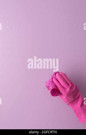 A hand in a pink protective rubber glove holds a microfiber cloth for washing on a purple background Stock Photo