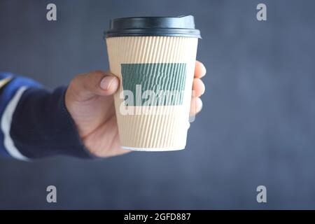 hand holding take away paper cup against black background. Stock Photo