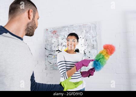 Cheerful african american woman pointing at dust brush near boyfriend Stock Photo