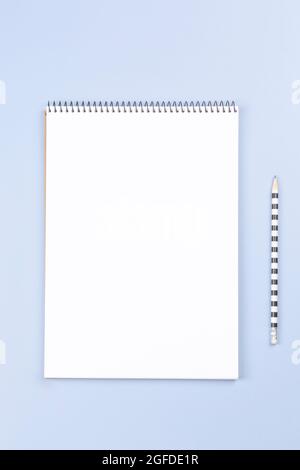 Open spiral notebook with blank white page and pencil on light gray desk background. Vertical top view, copy space for text Stock Photo