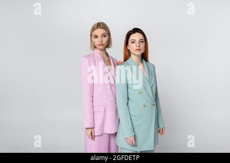 blonde and redhead women in pink and blue pastel suits posing isolated on grey Stock Photo