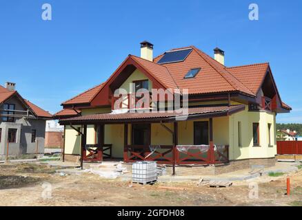 The construction of an energy efficient house with a complex cross gable roof with lightning protection and clay tiles, lightning rod, patio, stucco w Stock Photo