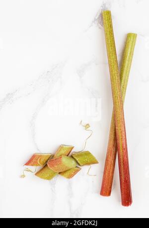 Fresh rhubarb stalks and sliced rhubarb on white marble worktop Stock Photo