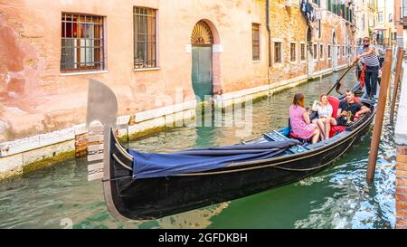 VENICE, ITALY - AUGUST 02, 2021: Tourists and gondolier on gondola boat. Romantic gondola cruise in Venetian water canal, Venice, Italy. Stock Photo