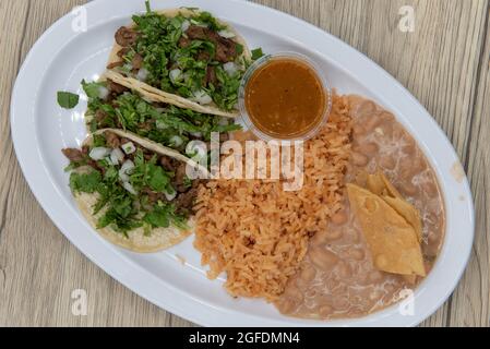 Overhead view of hearty plate of three loaded carne asada tacos with cilantro, served with rice and refried beans. Stock Photo