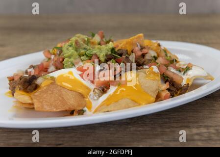 Hearty plate of nachos smothered with melted cheese, pico de gallo, and sour cream to serve as a meal. Stock Photo