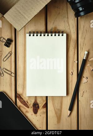 Top Table View, Open Blank Notebook On Wooden Desk With Open Cardboard Box, Camera Lens, Pencil, Mobile Phone, Flat Lay Copy Space For Text. Stock Photo