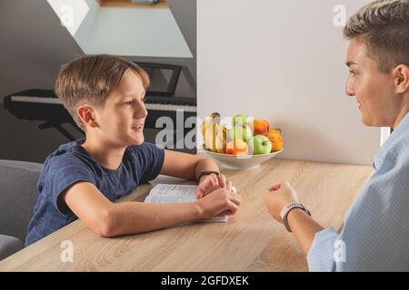 Kid boy doing homework at kitchen table with book Stock Photo