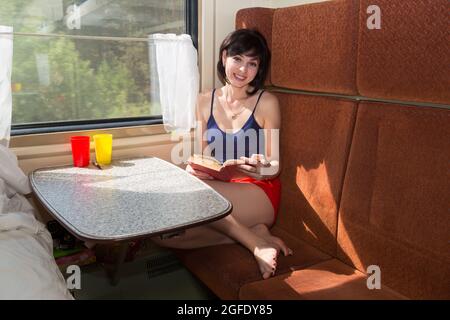 A brunette woman in a compartment car reads a book to pass the time on the road. Stock Photo