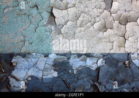 Old cracking paint on a two toned wall shows the concrete wall beneath Stock Photo