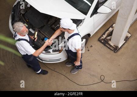 Top view shot of two car mechanics shaking hands over car hood Stock Photo