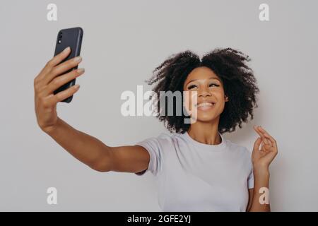 Positive cheerful dark skinned female making photo on modern smartphone camera Stock Photo