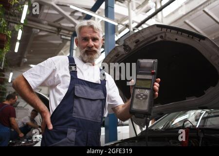 Senior car mechanic using computer to run auto diagnostics at the garage Stock Photo