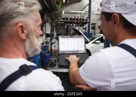 Close up rear view shot of two professional repairment using computer at car workshop Stock Photo