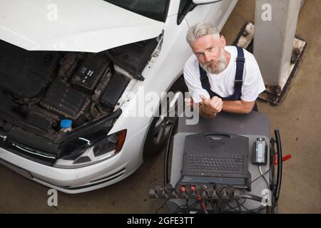 Top view shot of a senior car service worker using computer to check broken automobile Stock Photo