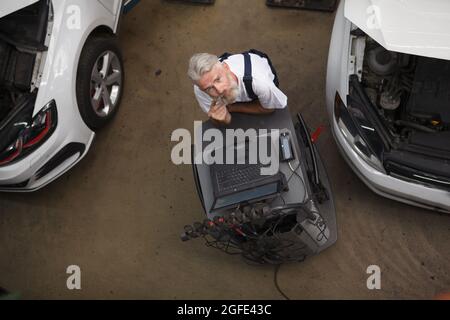 Senior car maintenance engineer working on computer at the garage Stock Photo