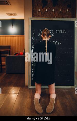 Young woman writing cafe menu on black desk chalkboard using chalk Stock Photo