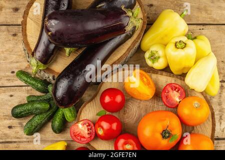 Assortment of fresh vegetables on a wooden background. Ripe tomatoes, eggplants, cucumbers and bell peppers, top view Stock Photo