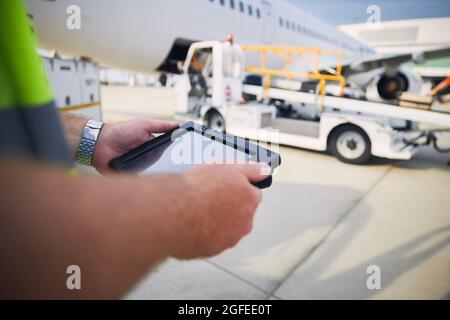 Member of ground staff preparing passenger airplane before flight. Worker using tablet against plane at airport. Stock Photo