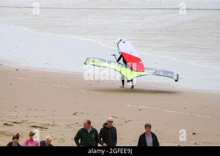 A person carrying a foil  board; that's a hydrofoil surfboard normally used in conjunction with a kite for propulsion, makes his/her way along Llangennith beach, Gower, Swansea, UK, toward the sea. Stock Photo