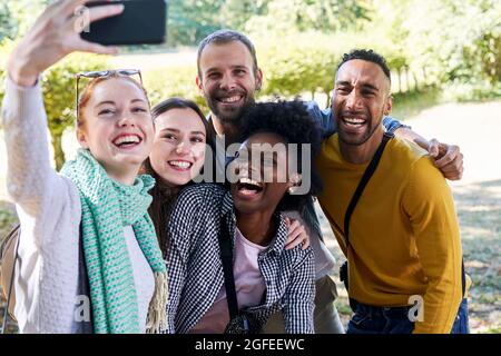 Smiling woman taking selfie with smart phone while standing with friends in park Stock Photo