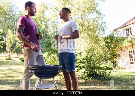 Young men with beer bottles standing near barbecue grill Stock Photo