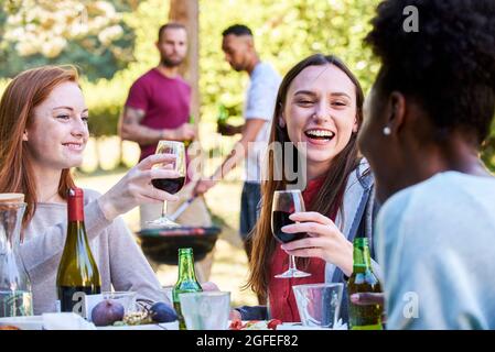 Smiling young women having wine and beer in park Stock Photo