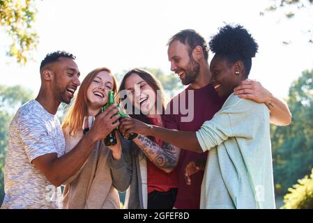 Smiling young friends standing with beer bottles and wine glass in garden Stock Photo