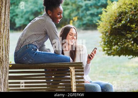 Smiling young friends using smartphone Stock Photo