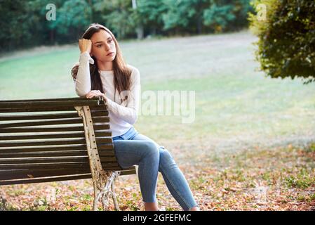 Thoughtful young woman sitting on bench in park Stock Photo