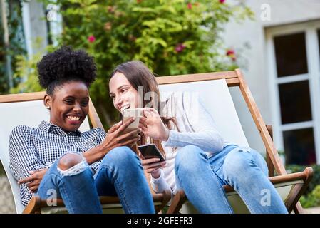 Smiling young friends using smartphones in park Stock Photo