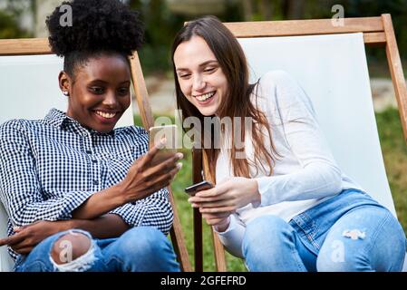 Smiling young friends using smartphones in park Stock Photo