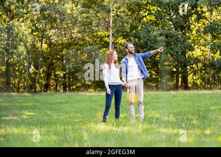 Smiling young man pointing something to his partner while standing in park Stock Photo
