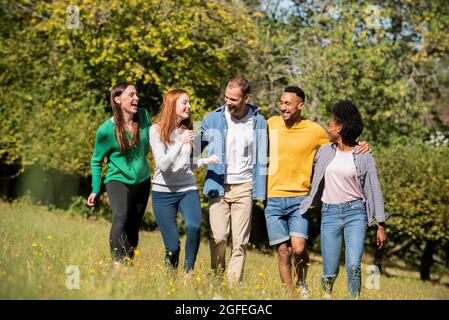 Happy young friends walking through meadow in public park Stock Photo