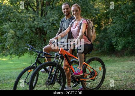 Portrait of smiling young couple sitting on bicycles in forest Stock Photo