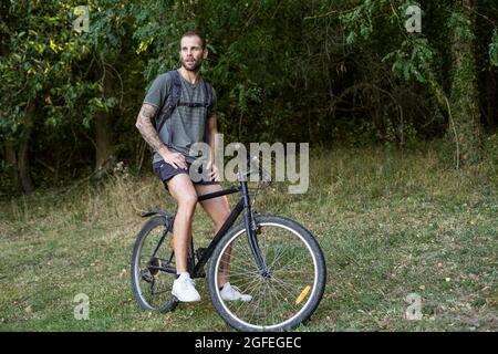 Thoughtful young man sitting on bicycle in forest Stock Photo