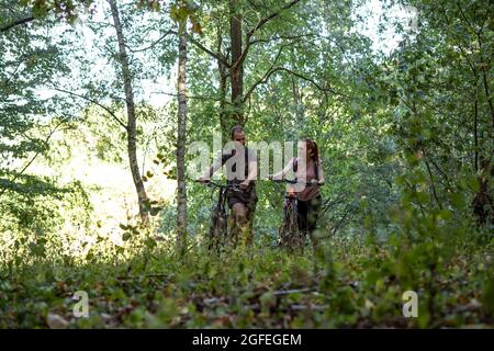 Smiling young couple walking with bicycles in forest Stock Photo