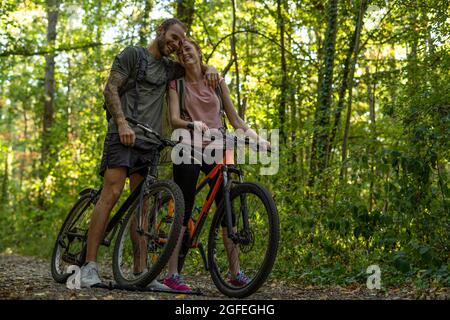 Smiling young couple standing with bicycles in forest Stock Photo